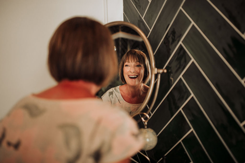 Mother of the bride makeup in Trogir Croatia, smiling at her reflection with natural and elegant bridal beauty look