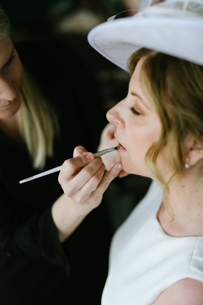 Mother of the bride wearing an elegant hat while receiving final lip touch-ups by Katarina Kate Ramic in Dubrovnik.